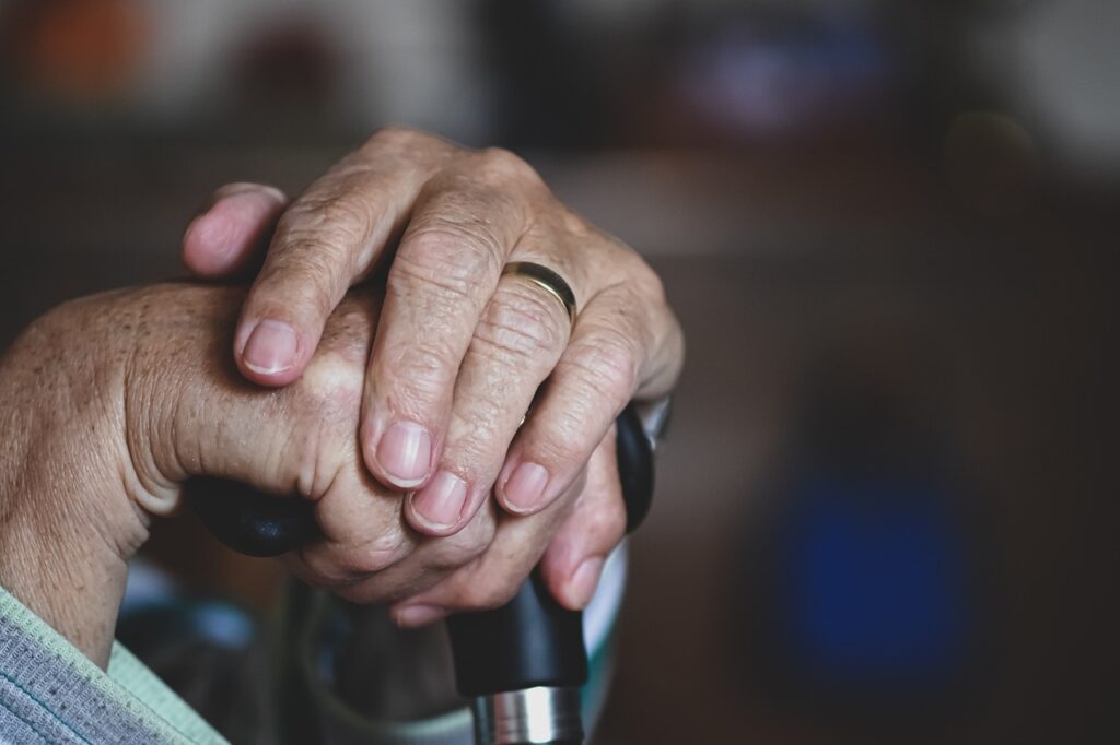Folded hands of elderly person with cane and wedding band