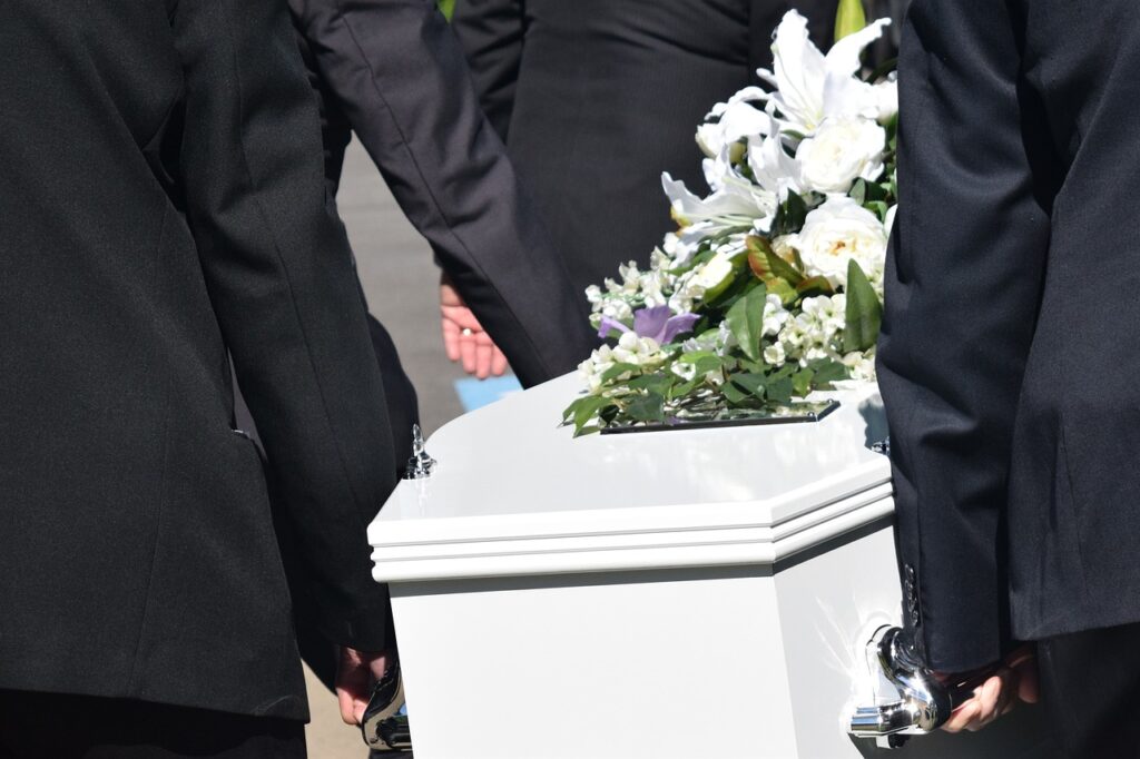 Pall bearers carrying white coffin covered with white flowers
