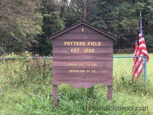 Image of wooden sign with the words Potters Field, Est 1800, set in a grassy field with trees in background