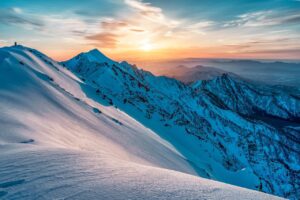 Snow-covered high mountain peaks with tiny human figure silhouetted on a ridge.