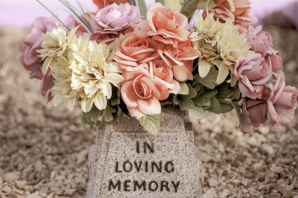 Photo of pink, white, and lavender flowers adorning a gravestone that say In Loving Memory