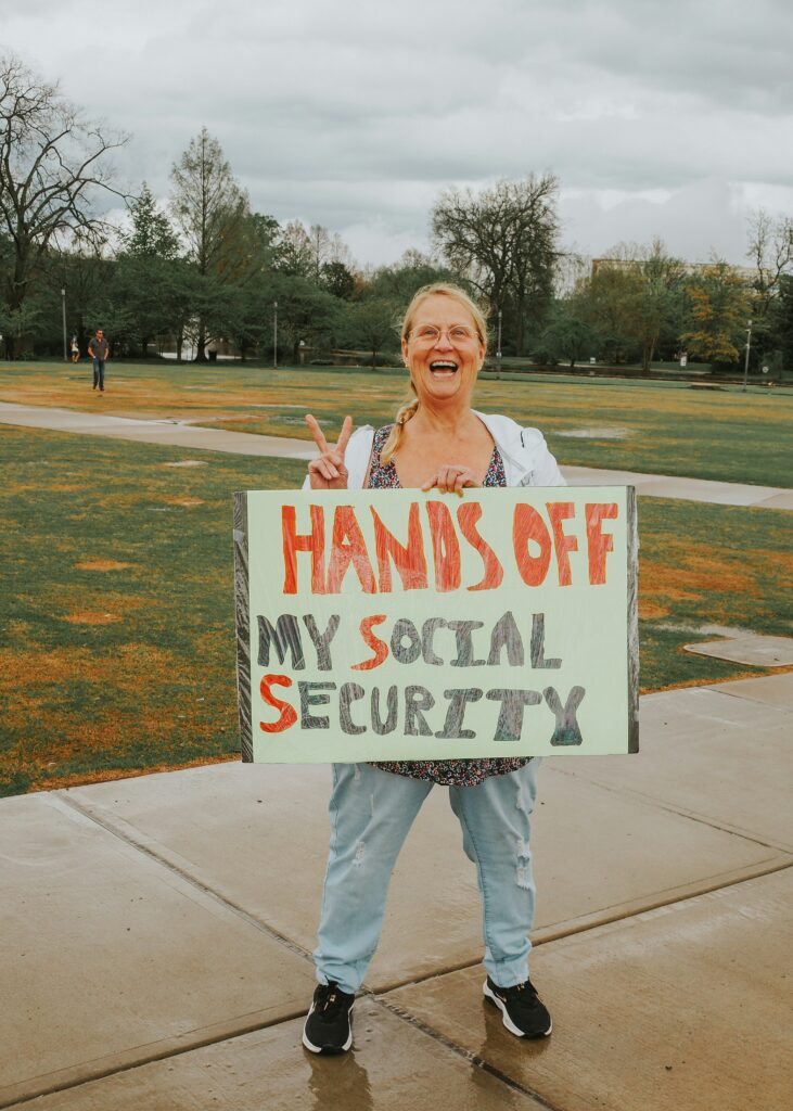 Photo of woman protesting with sign that reads hands-off-my-social-security