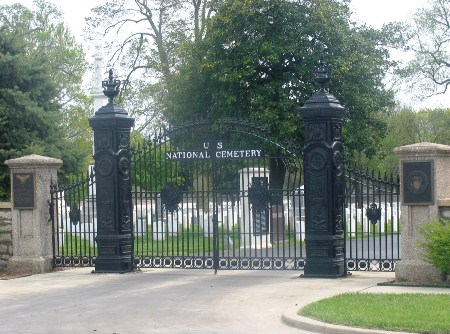 Photo of black metal gate labeled U.S. National Cemetery, with white gravestones visible behind the black gate